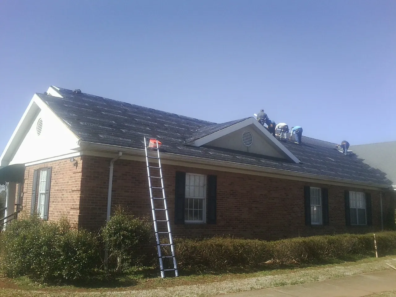 Crew tearing shingles off a brick ranch roof with a ladder set — Emergency Roof Repair work by our crew in Russells Point