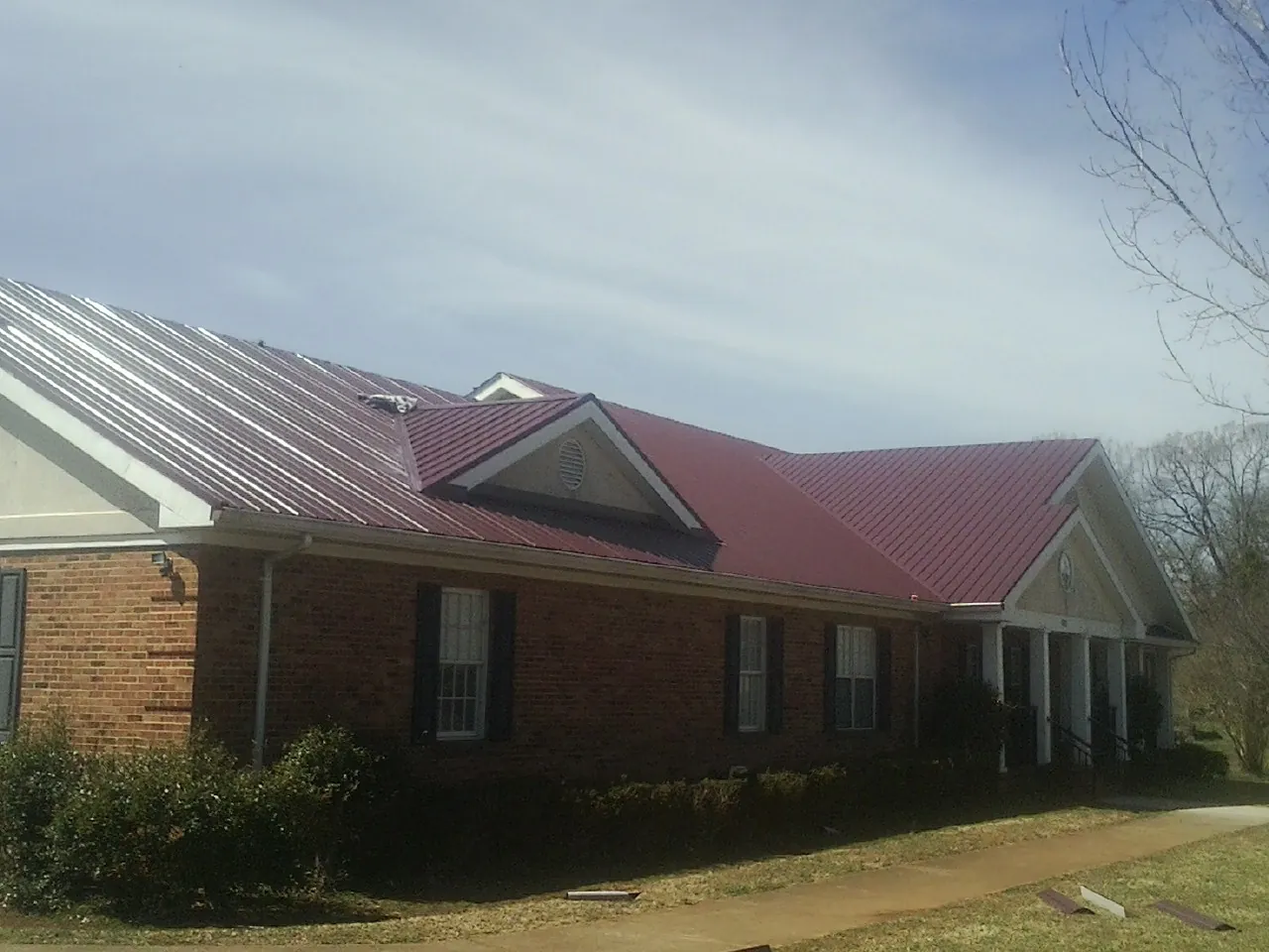 Red metal roof with gabled entries on a long brick building, from a Hail Damage Roof Repair job in Russells Point