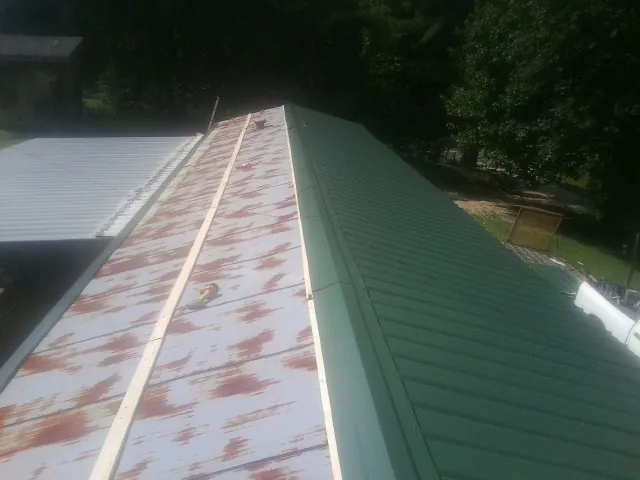 Old rusted panels beside newly installed green metal roofing — Wind Damage Roof Repair by Roofing Brothers in Russells Point
