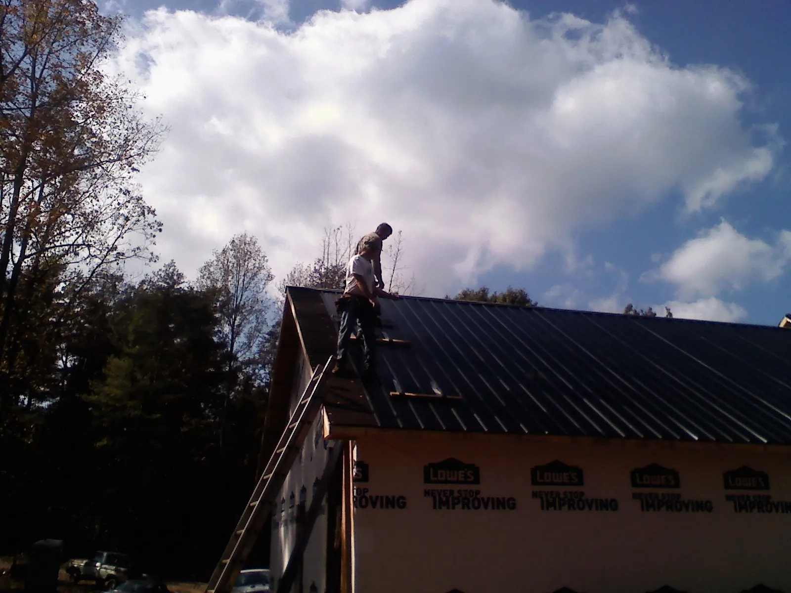 Roofer fastening dark metal panels high against a cloudy sky, from a Roof Inspection job in Russells Point