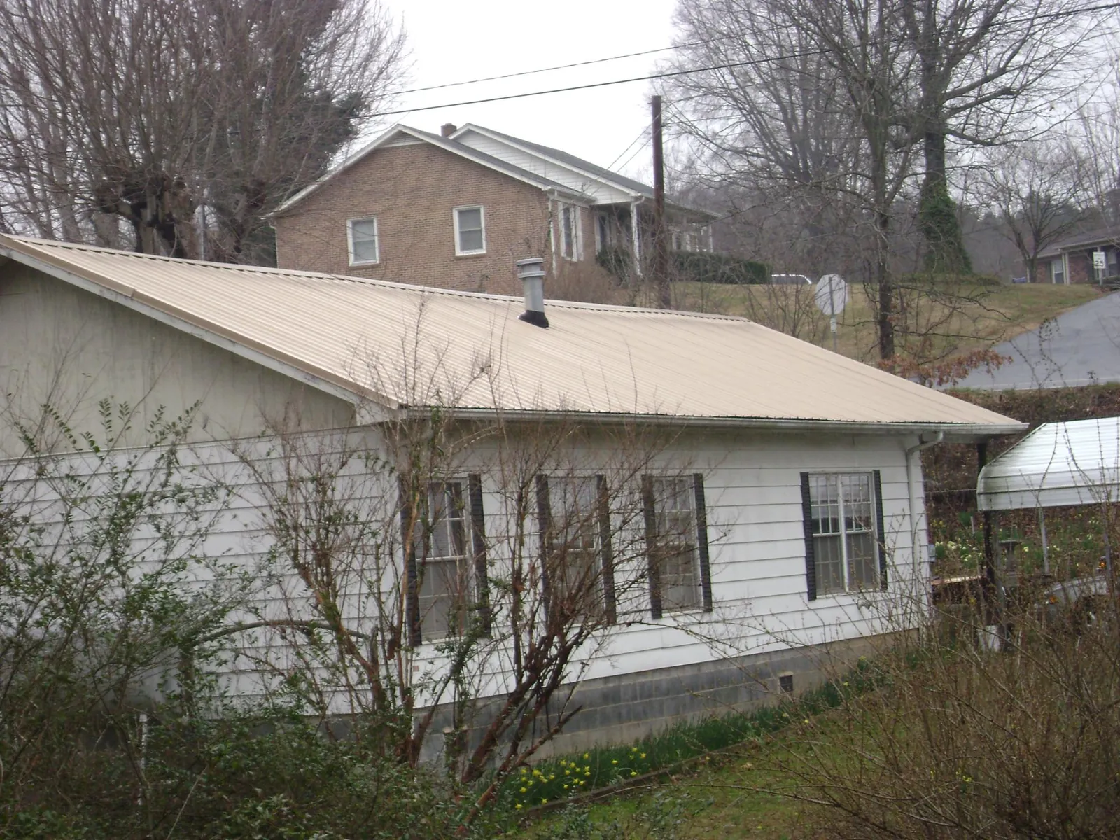 Tan metal roof on a white sided house set into a hillside — Commercial Roofing by Roofing Brothers in Russells Point