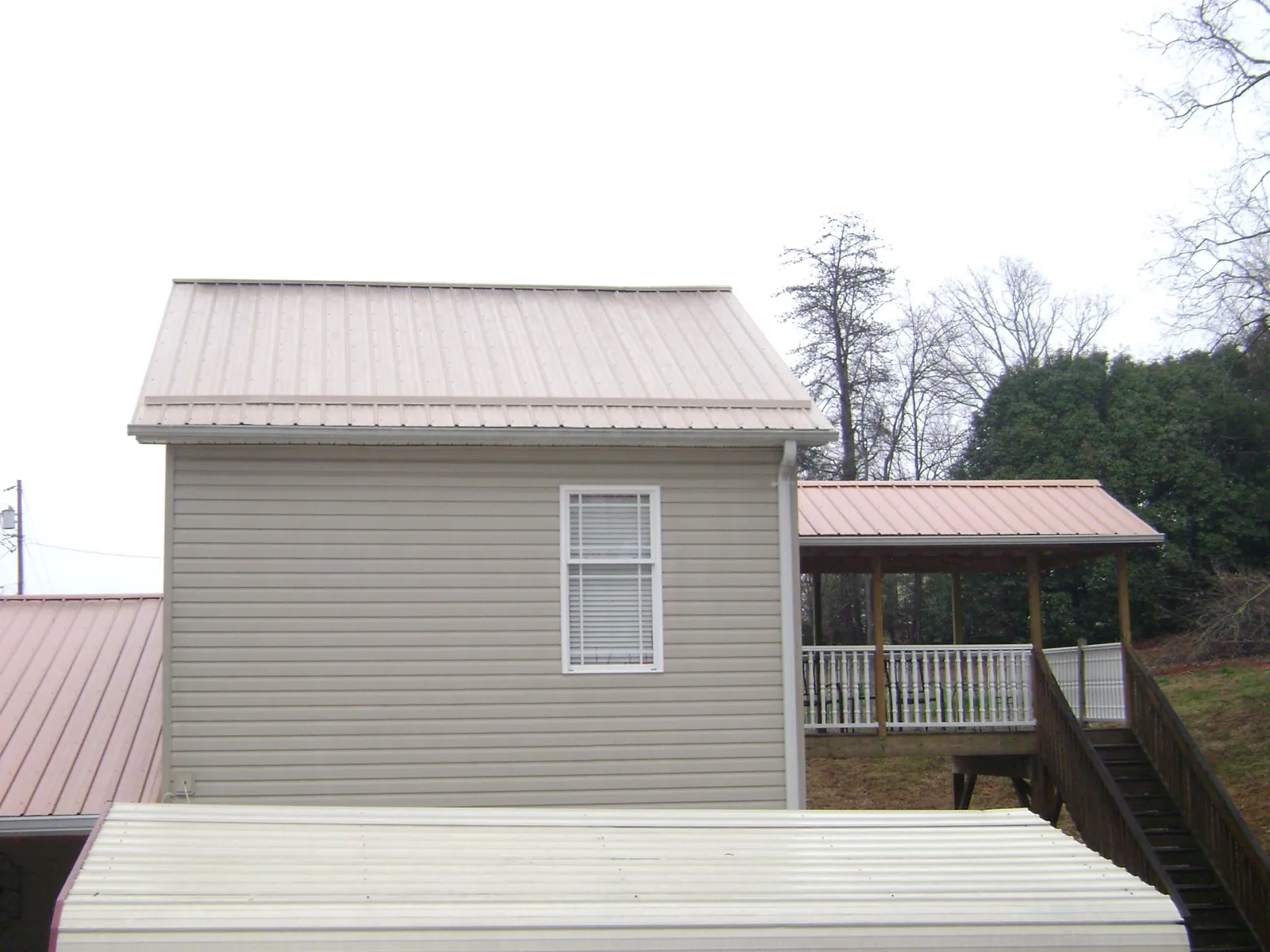 Tan metal roofs on a two story addition and attached porch, from a Roof Replacement job in Russells Point